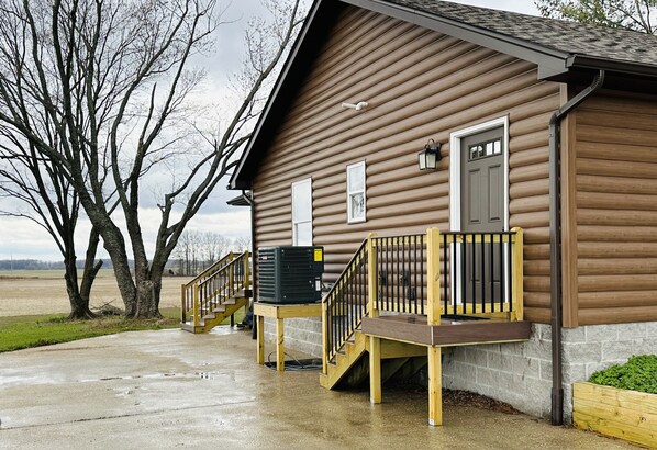 A wooden building with a porch, a staircase, and a large air conditioning unit.