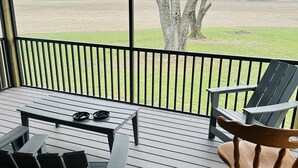 A covered outdoor seating area with a table and chairs, overlooking a field and a tree. - Outdoorsman Paradise (Wolf Lake)