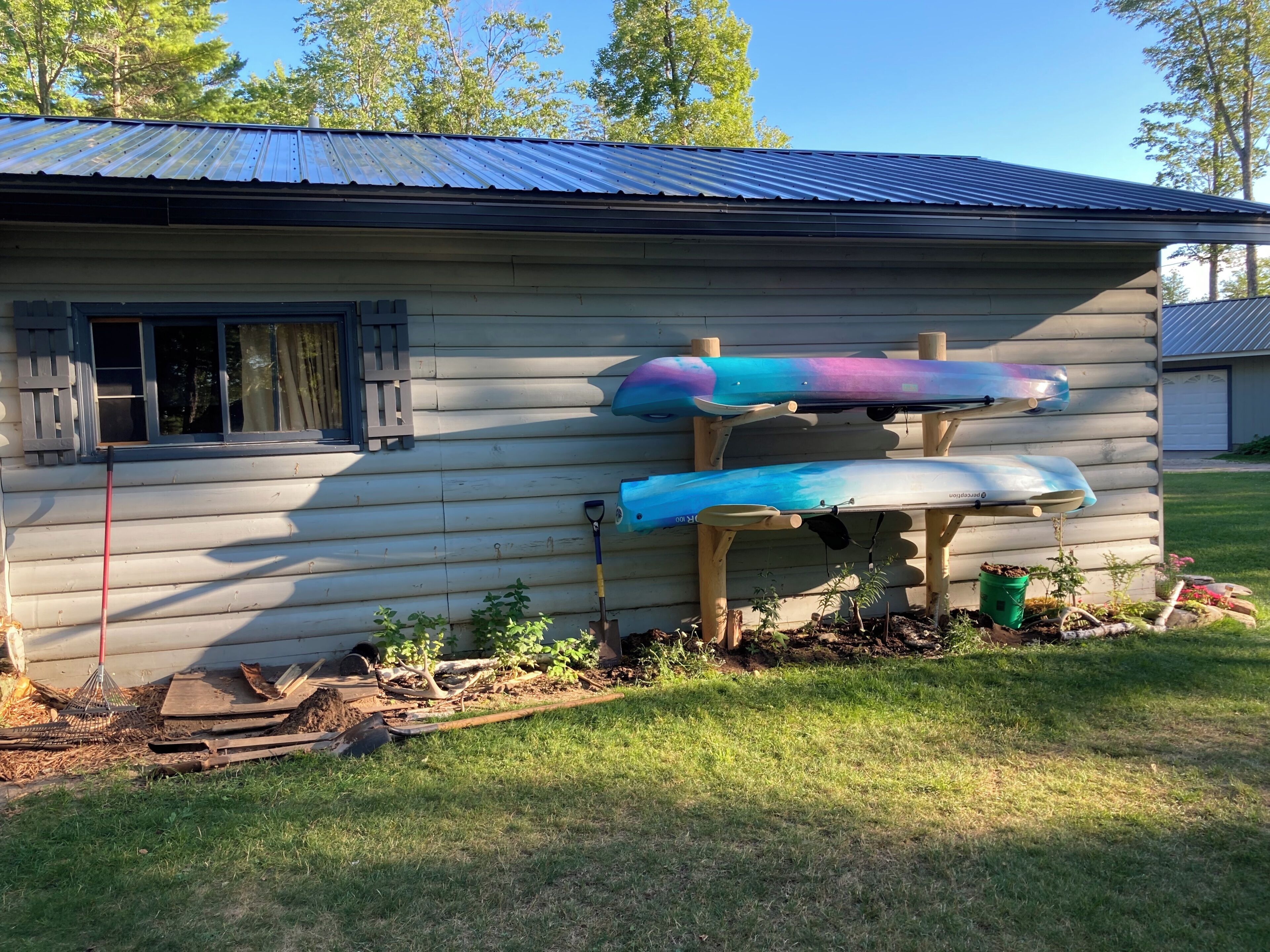 A log cabin with a metal roof, two kayaks mounted on a wooden stand, and a window with a curtain.