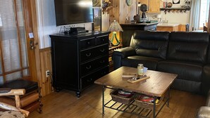 Un salón acogedor con techo de madera, un sofá de cuero negro, una mesa de centro de madera y un televisor.