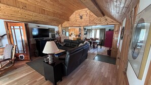 Un salón amplio con un sofá de cuero negro, techo de madera y un comedor con mesa y sillas.