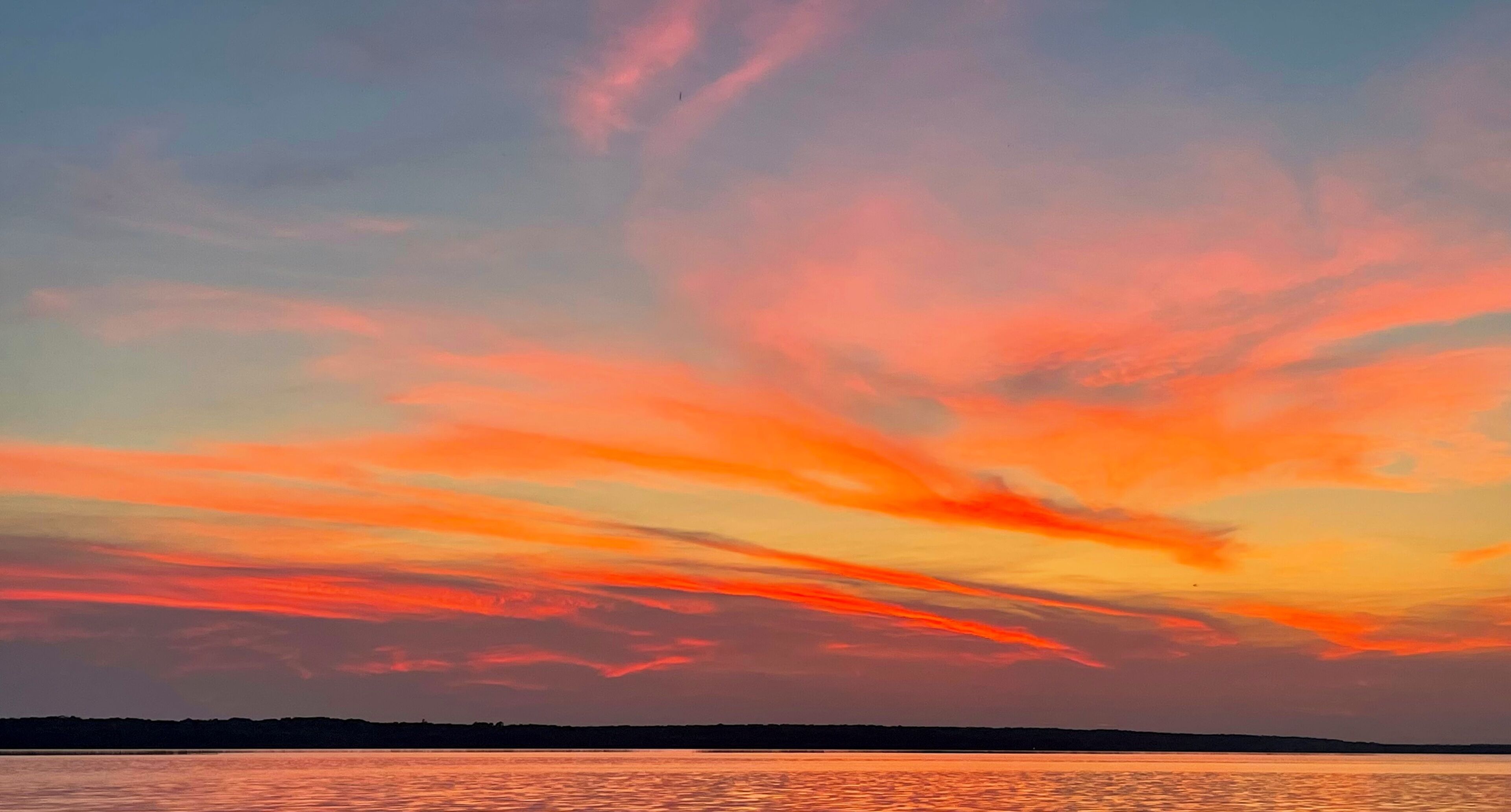 A sunset over a calm body of water with a silhouette of land in the distance.