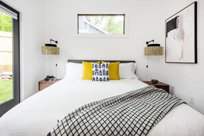 Quarto com cama grande, duas mesas de cabeceira, uma janela e luminária na parede.