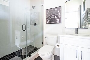 A modern bathroom with a glass shower enclosure, a white toilet, and a white vanity with a mirror. - Dapper Dan (Atlanta)
