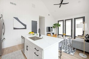 Uma cozinha moderna com bancada branca, pia embutida e ventoinha no teto.
