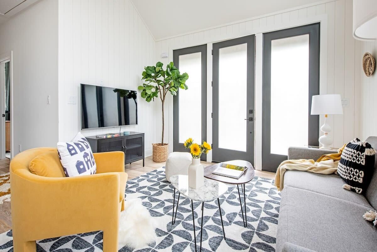 Ein Wohnzimmer mit einer Couch, einem Sessel, einem Couchtisch und einem Fernseher. Auf dem Tisch stehen eine Pflanze und eine Lampe.