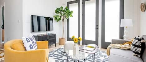A living room with a sofa, armchair, coffee table, and a TV. There is a plant and a lamp on the table.