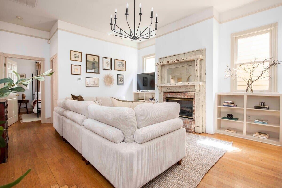 A living room with a large beige sofa, a fireplace, and a chandelier.