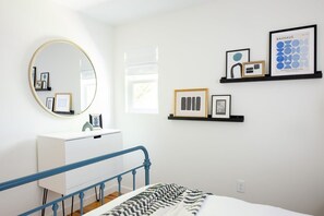 Un dormitorio con una cama, un espejo redondo, un aparador blanco y obras de arte enmarcadas en la pared.