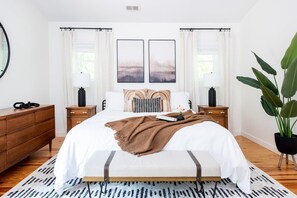 Ein Schlafzimmer mit einem großen Bett, zwei Nachttischen, einem Spiegel und einem Blumentopf.