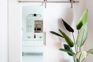 Baño blanco con espejo, tocador y planta.