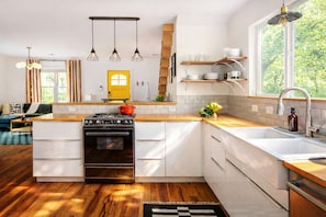 A modern kitchen with a central island, wooden flooring, and a view of greenery outside.