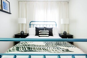 Une chambre à coucher avec un lit, deux tables de chevet et une fenêtre avec des rideaux.