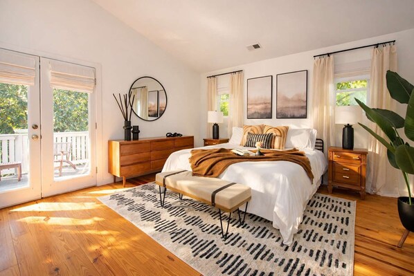 A bedroom with a large bed, wooden dresser, and a view of the outdoors through a sliding door.
