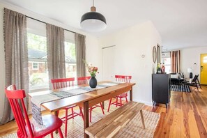 A dining area with a wooden table, red chairs, and a bench. There is a hanging light fixture above the table. - Cherry Cola (Atlanta)