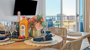 Ein Esstisch, gedeckt mit Orangensaft, Champagner, einer Blumenvase und Blick auf die Stadt durch große Fenster.