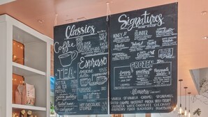 Ein Café mit einer Kreidetafel, die Kaffee- und Teeangebote auflistet, einer Vitrine mit Gebäck und einer Bar.