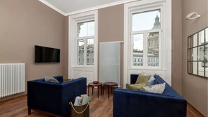 A living room with two blue sofas, a small round table, a radiator, and a television on the wall. - Venus Apartments - Italian Stylish (Budapest)