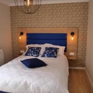 A bed with a blue headboard, two pillows, and two wall-mounted lamps.