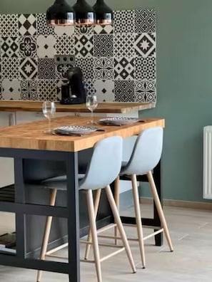 A kitchen with patterned tiles, a wooden island with chairs, and a coffee machine.