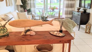 A living room with a wooden table, a sofa, a television, and a view of the outdoors. - “Cottage-Like” 2 Beds/2 Bath Condo Close To Beaches & The Heart Of ‘Old Stuart' (Stuart)