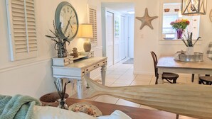 A cozy, well-lit room with a wooden dining table, a bench, and a large clock on the wall. - “Cottage-Like” 2 Beds/2 Bath Condo Close To Beaches & The Heart Of ‘Old Stuart' (Stuart)