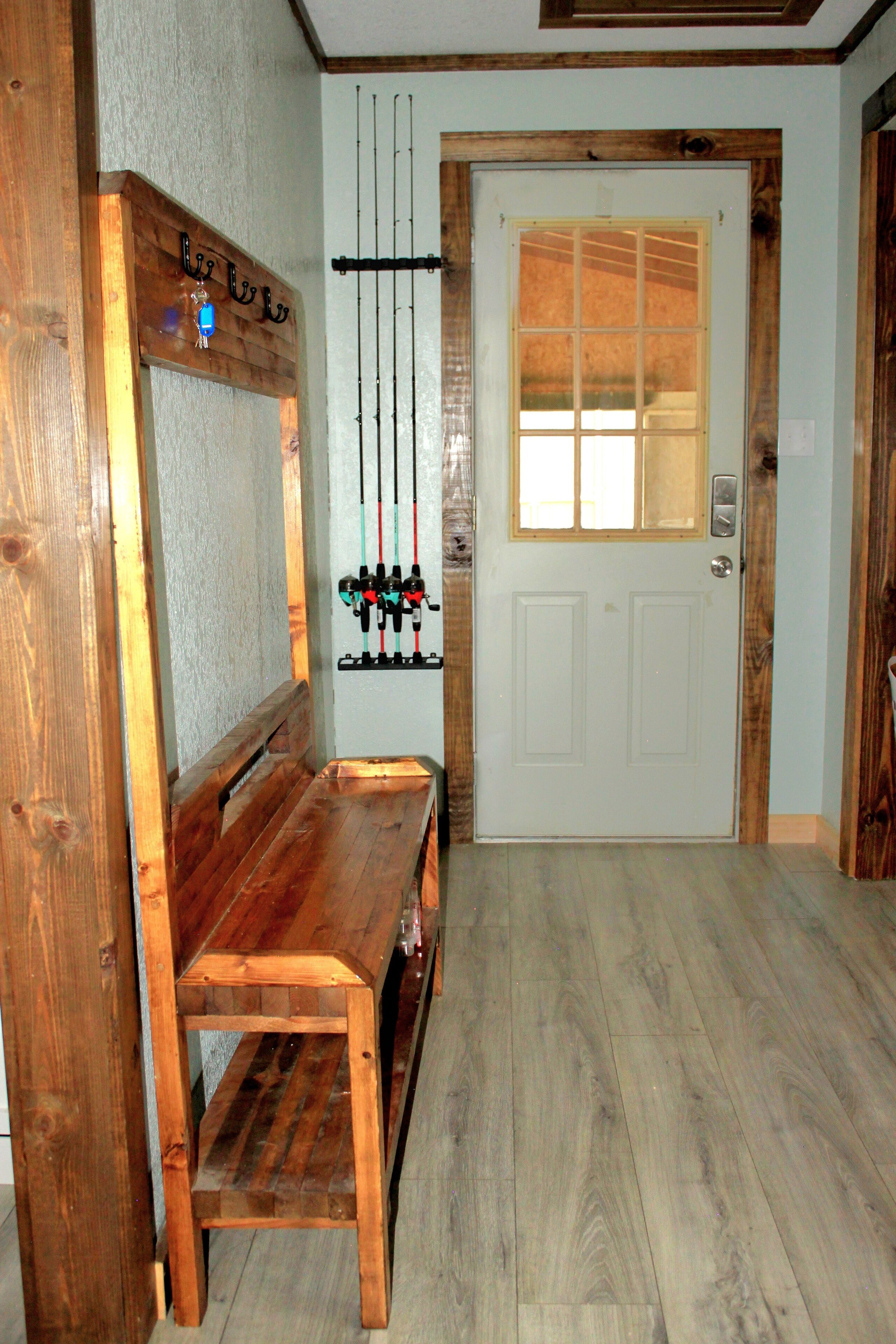 A wooden bench with a metal rack holding fishing rods in a room with wooden flooring and a white door with a window.