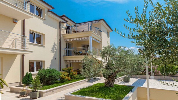 A multi-story residential building with balconies, a garden area with various plants, and a clear blue sky. - Holiday apartment with air conditioning and sea view (Selce)
