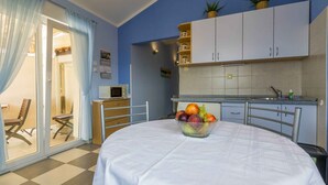 A room with a dining table, a bowl of fruit, a kitchen area with cabinets, a microwave, and a sliding glass door leading to a balcony. - Holiday apartment with air conditioning and sea view (Selce)