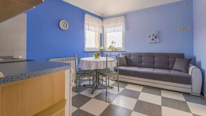 A room with a blue wall, a grey sofa, a round table with two chairs, a clock, and a window with white curtains. - Holiday apartment with air conditioning and sea view (Selce)