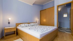 A bedroom with a wooden bed, two bedside tables with lamps, a wardrobe, and a checkered floor. - Holiday apartment with air conditioning and sea view (Selce)
