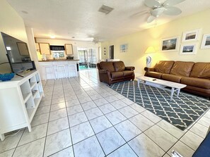 Relax in this inviting living area with a comfortable sofa, coffee table, and patterned rug, complemented by a modern kitchen with a central island and bar stools.