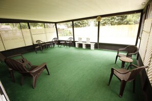 Relax in a sheltered outdoor space with a green turf floor, comfortable seating, and a small table.