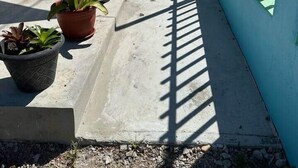 A covered outdoor corridor with potted plants, a concrete floor, and blue walls with barred windows. - Cayo Vieques at Almendro Guest House (Lajas)