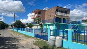 A two-story building with a balcony on the upper floor, a blue fence, and two large barrels near the entrance. - Cayo Vieques at Almendro Guest House (Lajas)