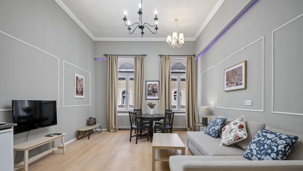 A modern living room with a flat-screen TV, a sofa, a dining table with chairs, and a chandelier. - Venus Apartments - Akacfa street I (Budapest)