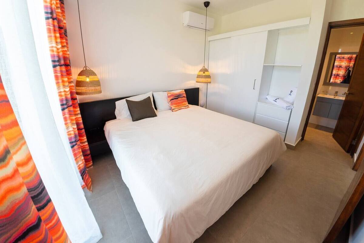 A hotel room with a large bed, two bedside lamps, a wardrobe, and a bathroom visible through an open door.