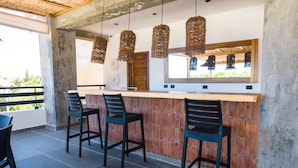 A bar area with a brick wall, hanging wicker light fixtures, and a wooden counter. - Surf N Roll Performance Center (Cabarete)