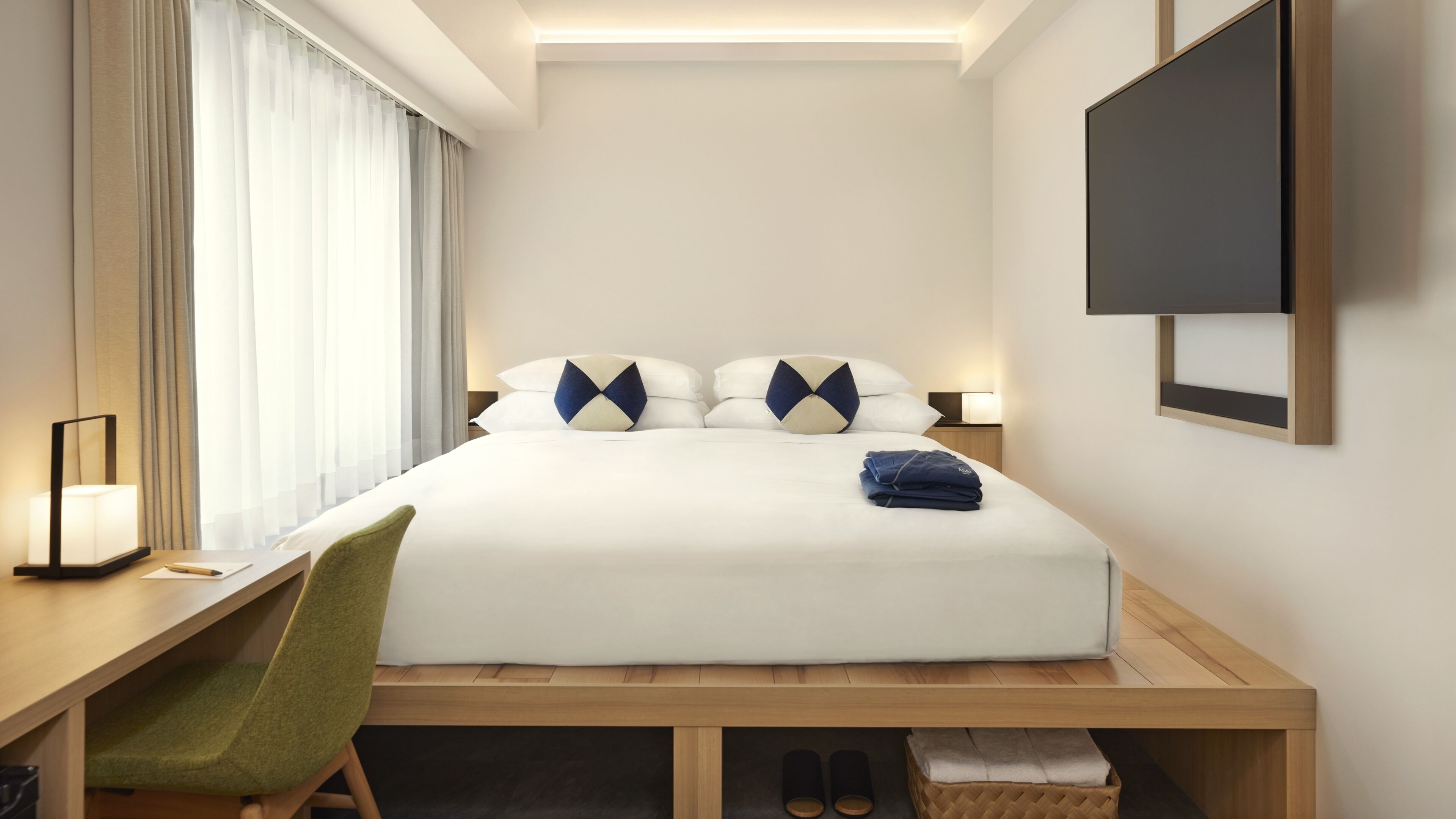 A hotel room with a bed, a desk, a chair, a TV, and a window with curtains.