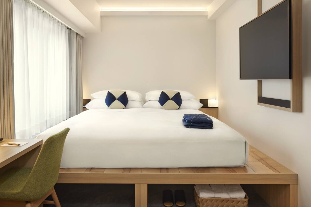 Ein Hotelzimmer mit Bett, Schreibtisch, Stuhl, Fernseher und einem Fenster mit Vorhängen.