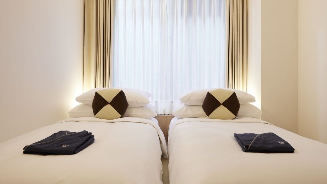 A hotel room with two beds, each with a pillow and a folded item on the bed.