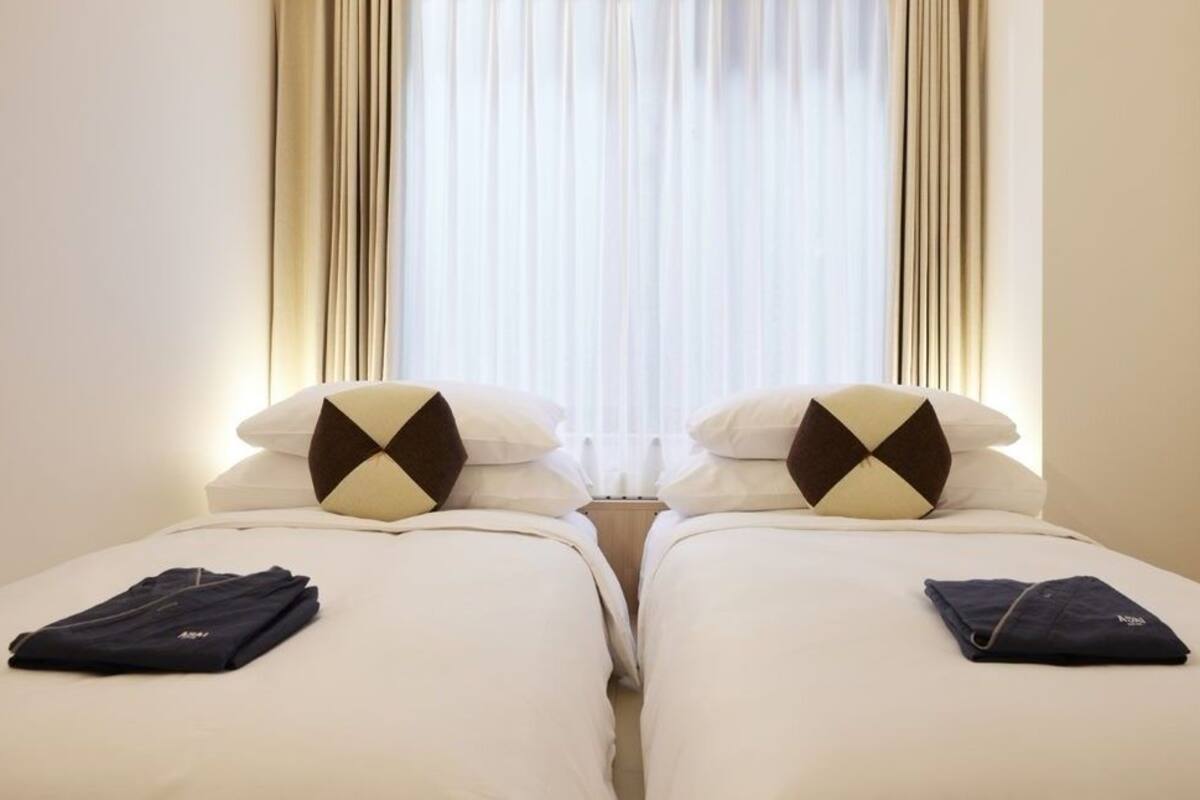 Ein Hotelzimmer mit zwei Betten, jedes mit einem Kissen und gefalteter Kleidung.