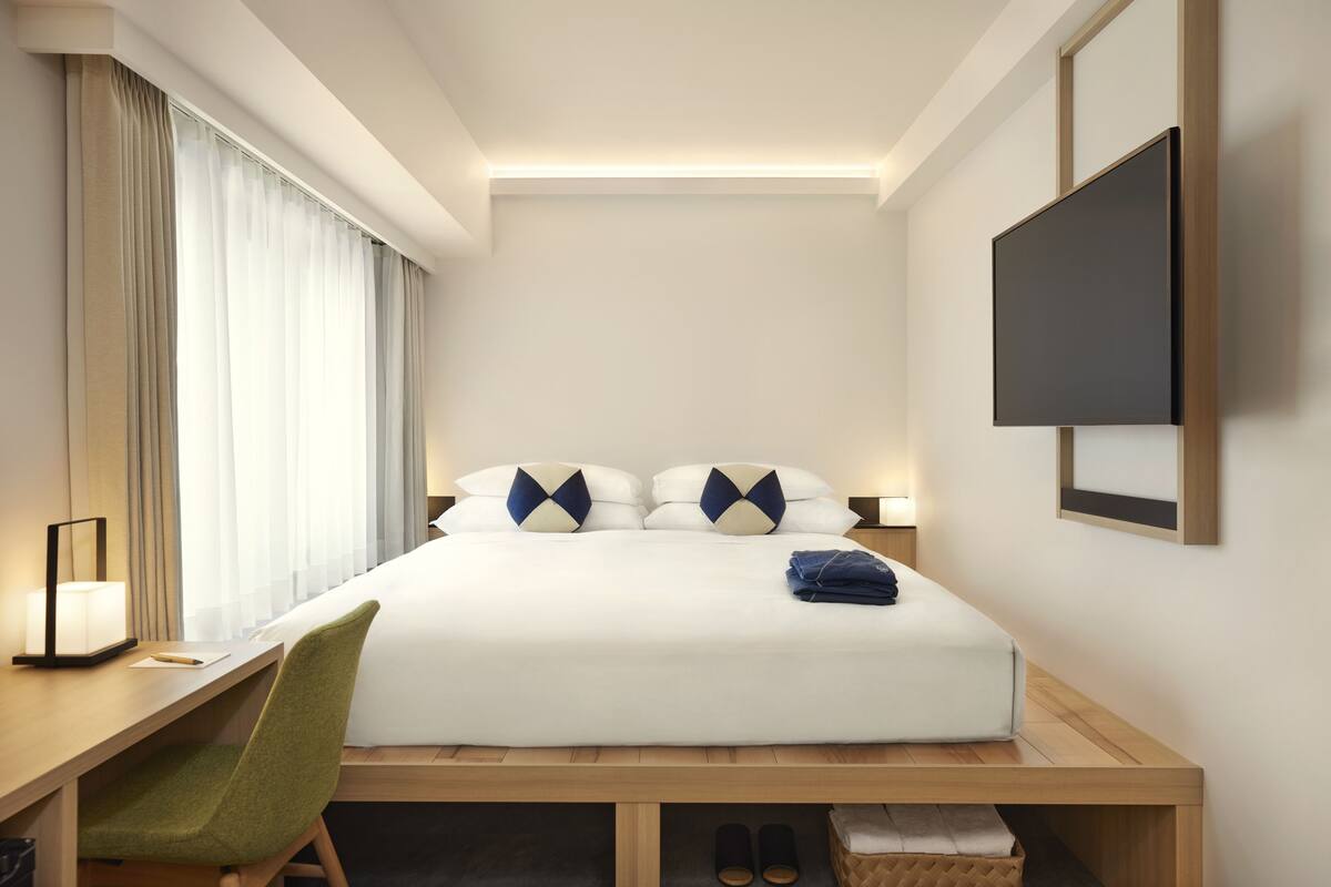 Ein Hotelzimmer mit Bett, Schreibtisch, Stuhl, Fernseher und einem Fenster mit Vorhängen.