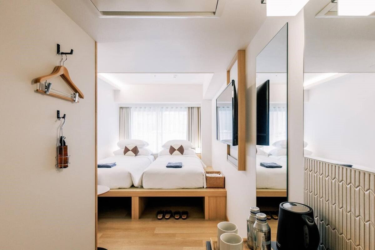 Ein Hotelzimmer mit zwei Betten, Holzboden, einem Schreibtisch mit Wasserkocher und einem Spiegel.