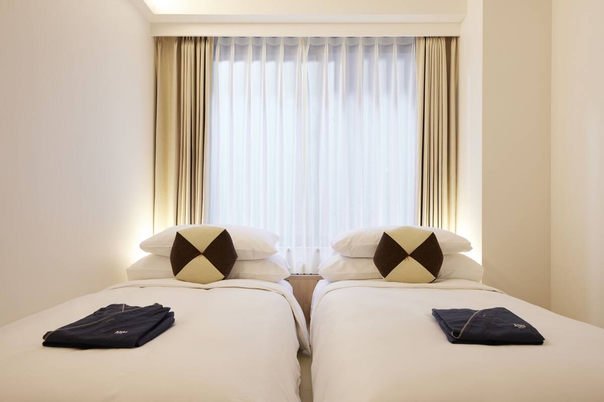 Ein Hotelzimmer mit zwei Betten, einem Fenster mit Vorhängen und einem Nachttisch.