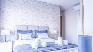 Une chambre d’hôtel avec un lit, deux tables de chevet, une petite table et une bougie bleue.