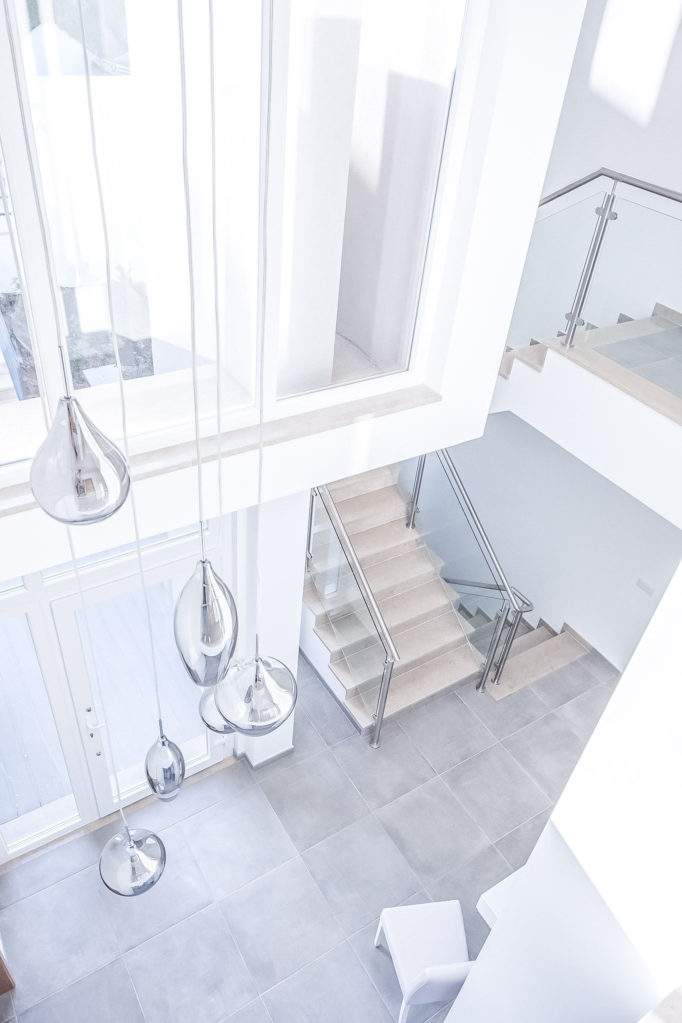 Un intérieur moderne avec un escalier en verre, des rampes en métal et des luminaires suspendus.
