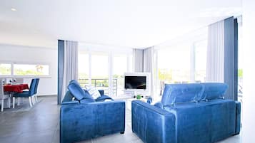 A modern living room with two blue sofas, a dining area with a red tablecloth, and a TV on a stand.