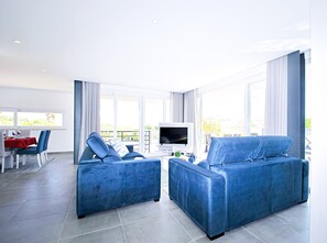 A modern living room with two blue sofas, a dining area with a red tablecloth, and a TV on a stand. - Luxury Villa w/ Jacuzzi and Heatable Pool (Armação de Pêra)