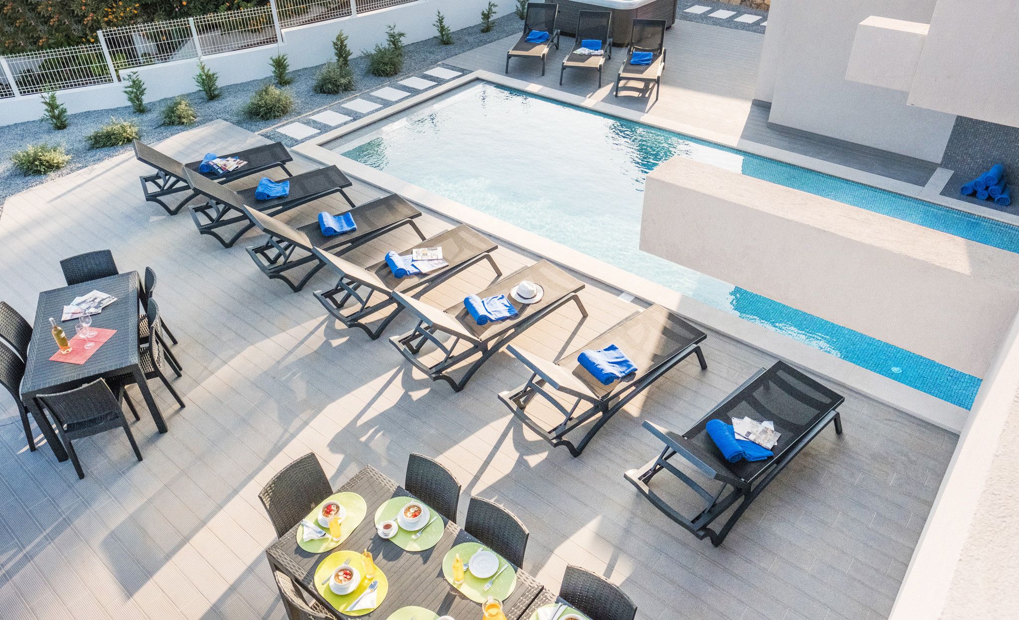 A rooftop pool area with lounge chairs, tables, and a dining setup.